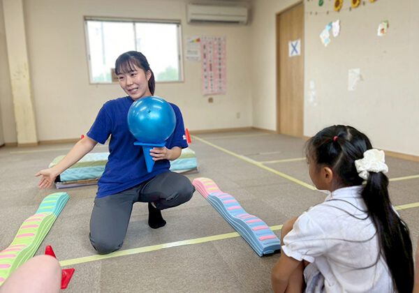 あそび王国：女性スタッフが子どもとボールを使った遊びを説明する様子。